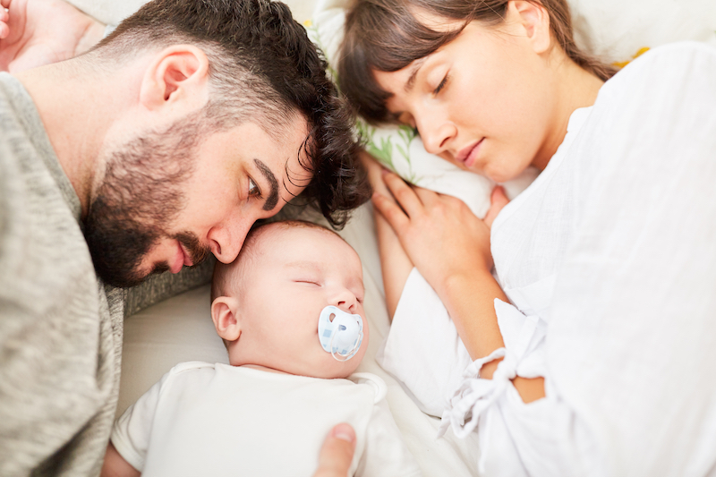 parents asleep on bed with baby before doing sleep training