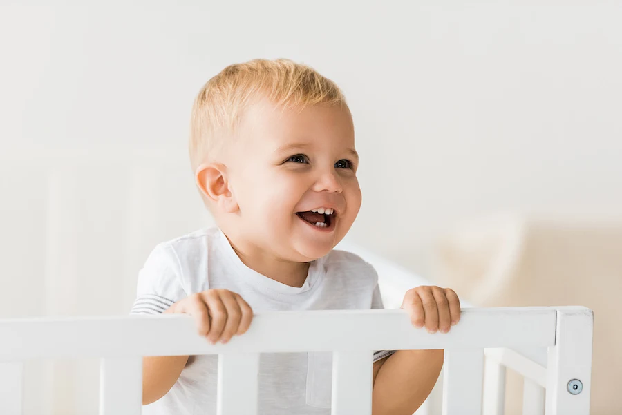 18 month old toddler happy in his crib 
