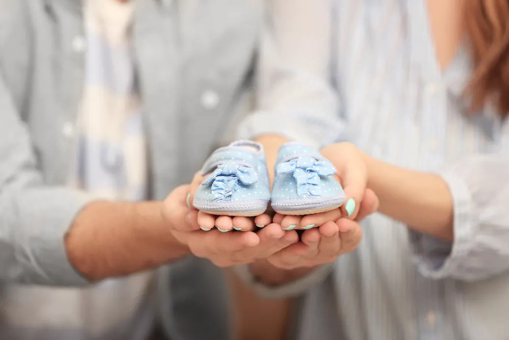 man and woman holding baby shoes to announce pregnancy