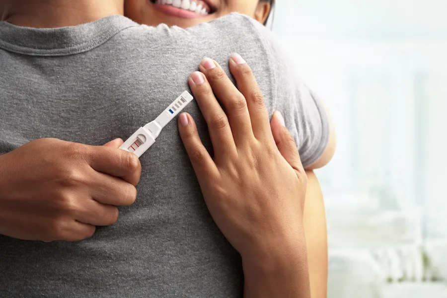 woman hugging man with positive pregnancy test on his back - what to do when you find out you're pregnant