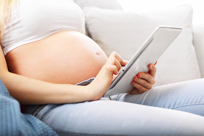 pregnant woman holding tablet on couch with her belly showing