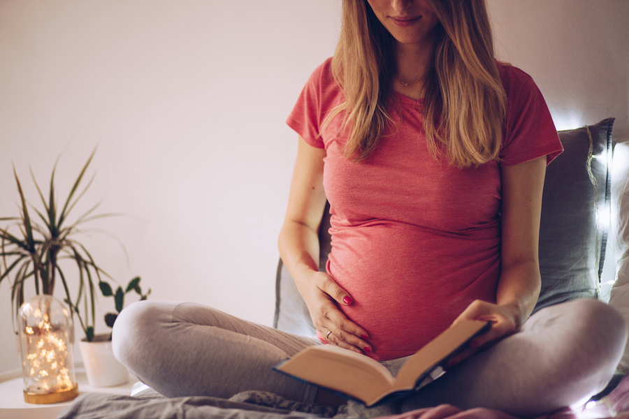 pregnant woman reading book - what to do when you find out you're pregnant