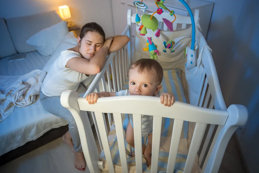 new mom laying on baby's crib during common sleep regressions
