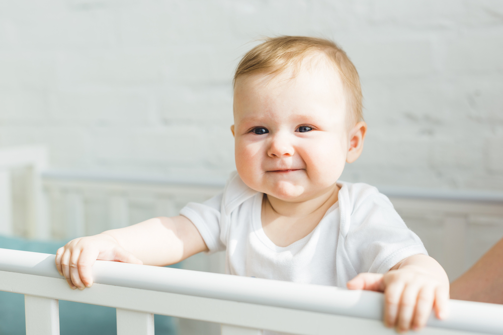 baby standing up and smiling in crib