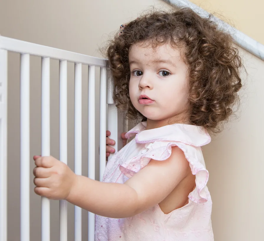 toddler sitting at baby gate when transitioning to toddler bed