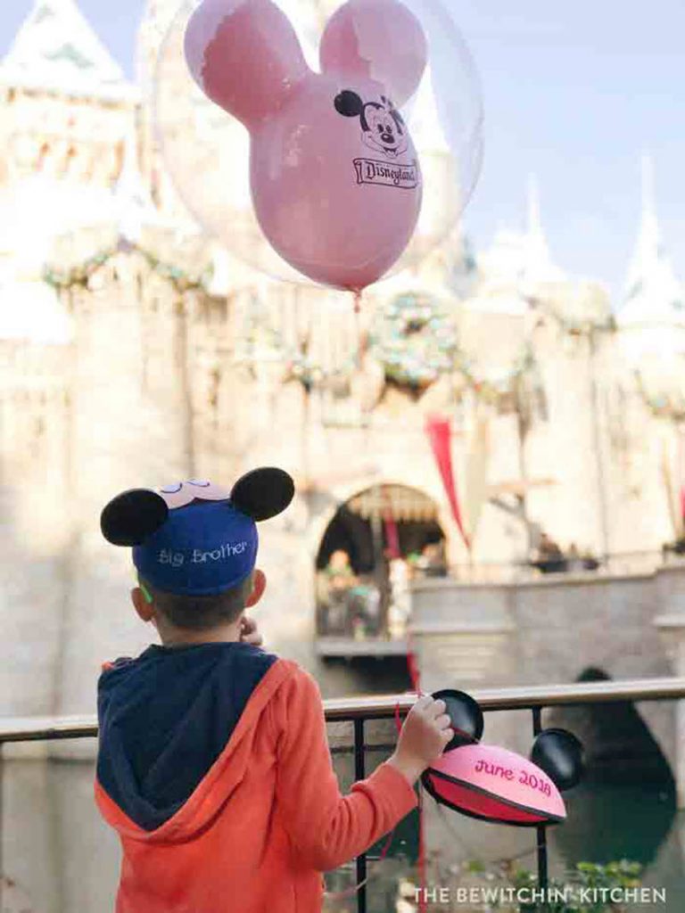 little boy holding balloon at Disney land and wearing big brother hat