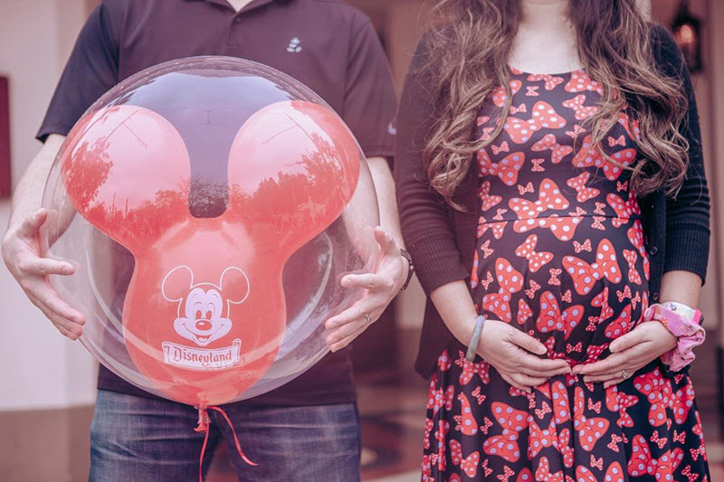 Disney pregnancy announcement - man holding Mickey Mouse balloon and woman holding pregnant belly