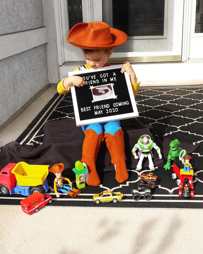 Disney pregnancy announcement - Boy dressed as Woody with Tiy Story friends surrounding him and pregnancy announcement on letter board