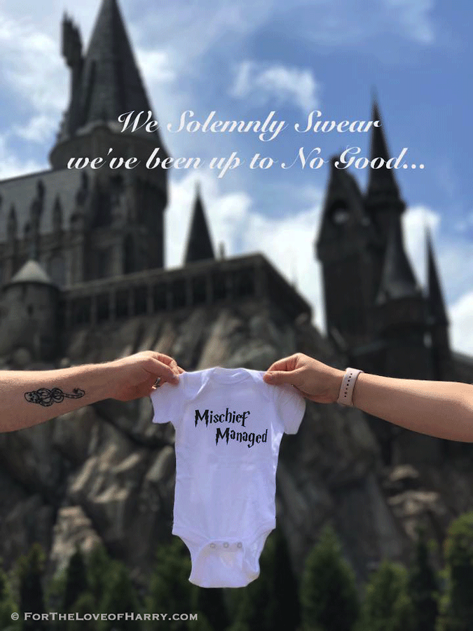 Mischief Managed baby bodysuit being help up in front of Hogwarts castle for Harry Potter pregnancy announcement