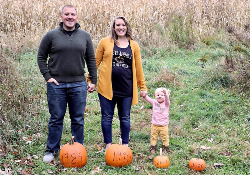 family at pumpkin patch announcing pregnancy