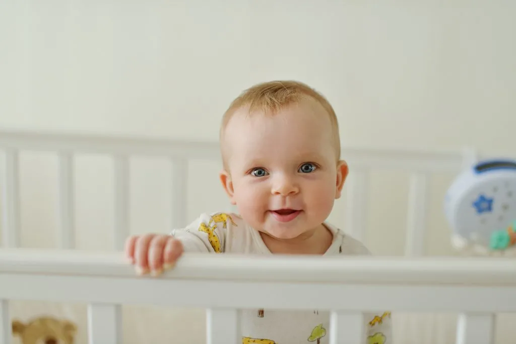 baby standing in crib smiling