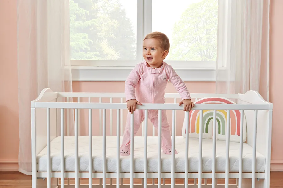 little girl standing up in her crib smiling