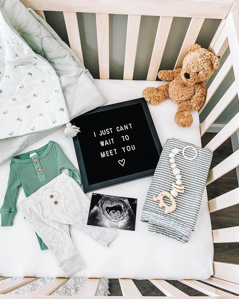 letter board pregnancy announcement in a crib with teddy bear
