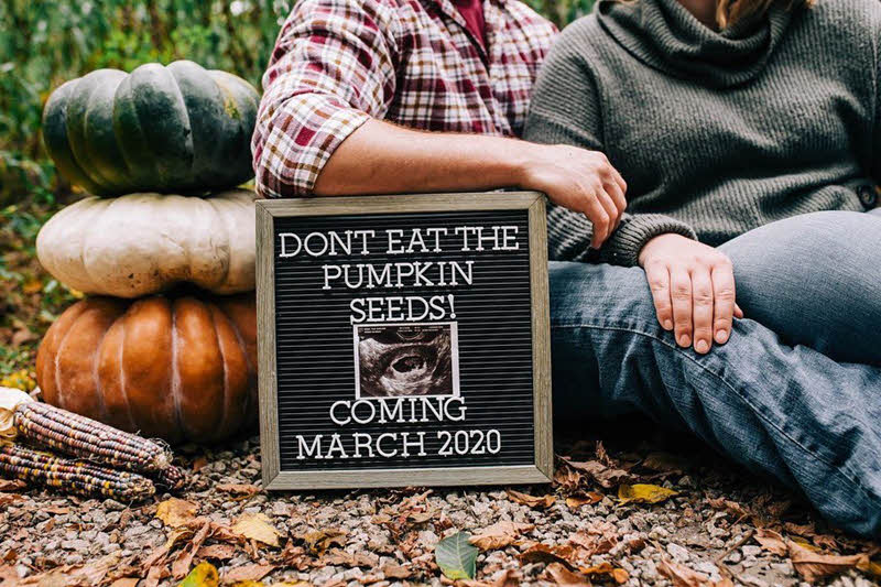 couple posing with letterboard and pumpkins to announce pregnancy