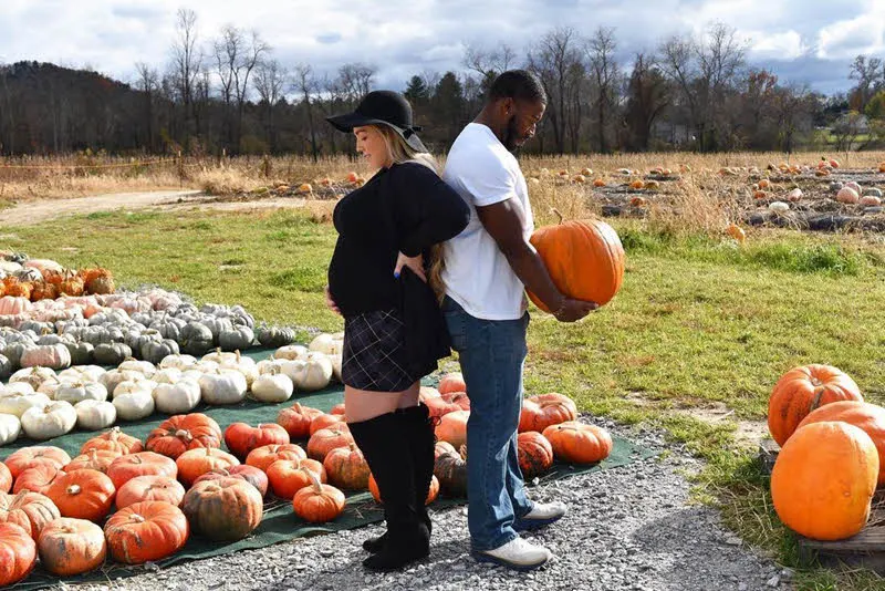 couple holding pumpkins on belly for a fall pregnancy announcement
