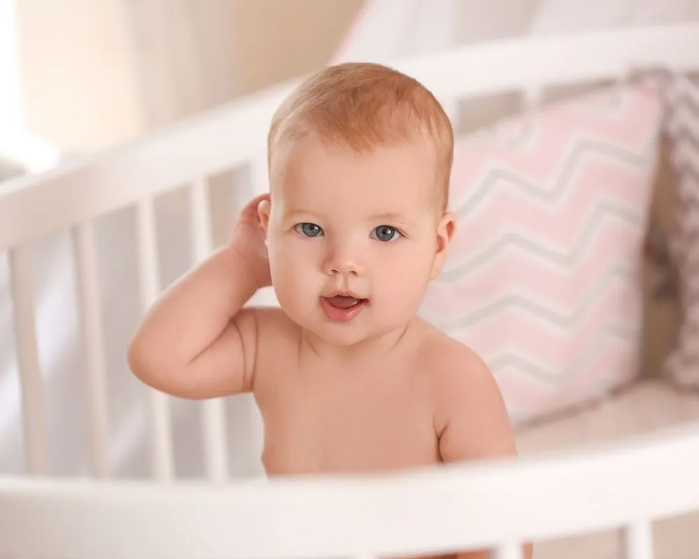 baby girl sitting up in crib - physical milestones can cause 6 month sleep regression