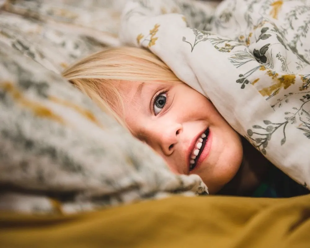 toddler peeking through comforter in bed