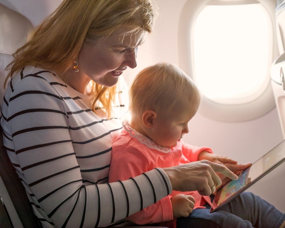mom and baby traveling on an airplane looking at a tablet