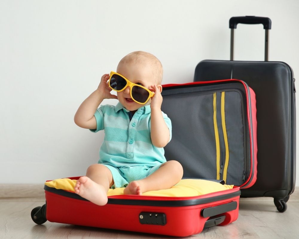 baby sitting on top of luggage with sunglasses