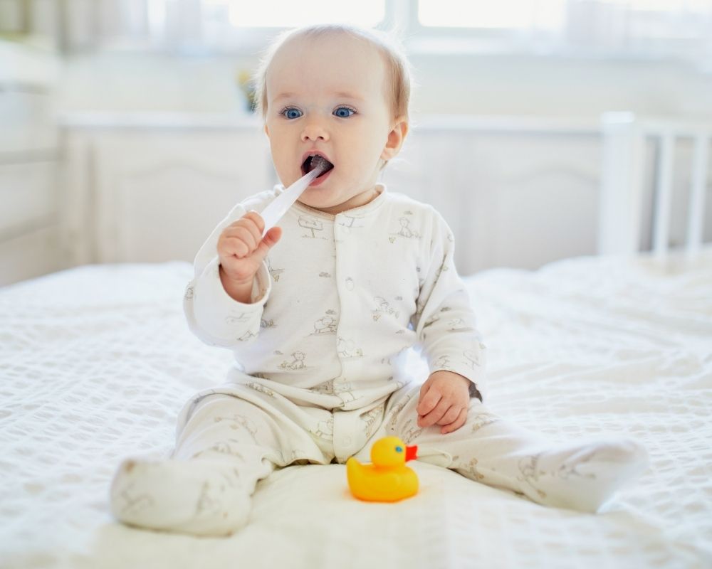 baby dressed in footed pajamas brushing teeth
