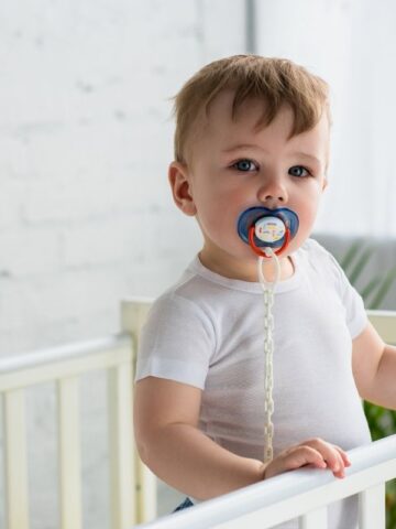 baby standing in crib with pacifier in mouth