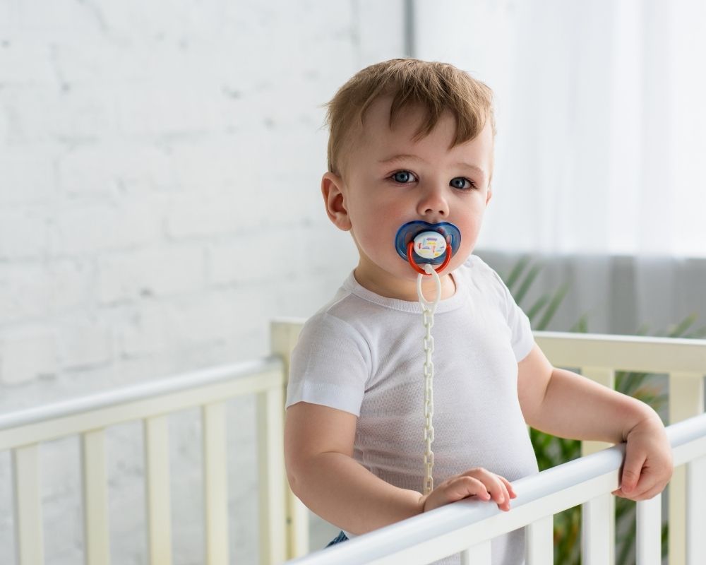 baby standing in crib with pacifier in mouth