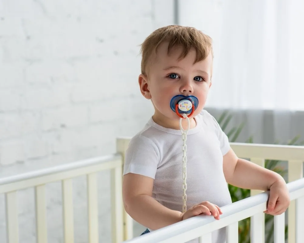toddler standing in crib with pacifier in mouth