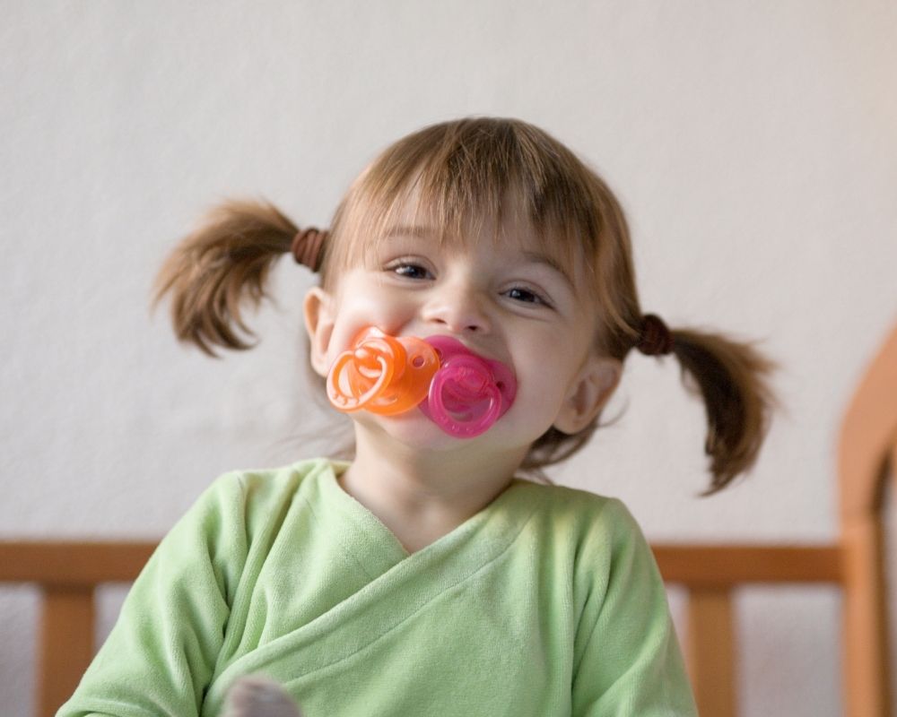 toddler girl with multiple pacifiers in mouth