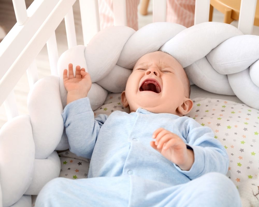Baby in crib crying with bumpers 
