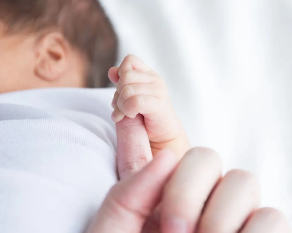 Sleeping newborn holding parents' finger