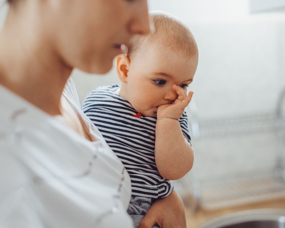 mom holding baby while baby sucking thumb