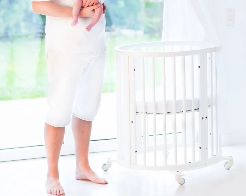 Parent holding baby next to a small bassinet
