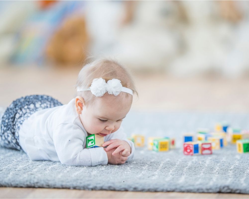 baby girl holding blocks while playing on the ground