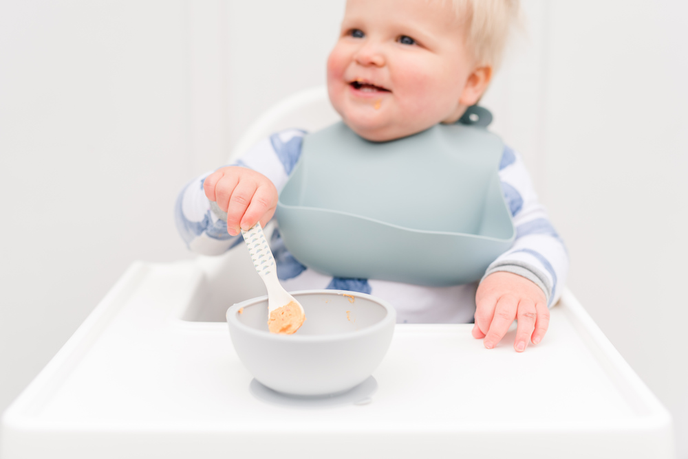 baby sitting in high chair with spoon and bowl