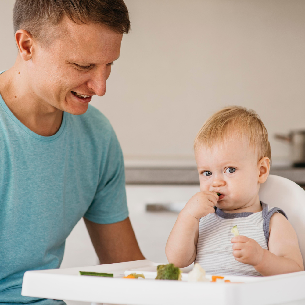 baby in highchair feeding himself and dad sitting next to baby