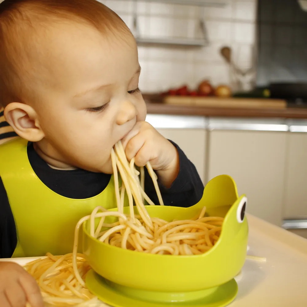 baby feeding self a fistful of spaghetti noodles