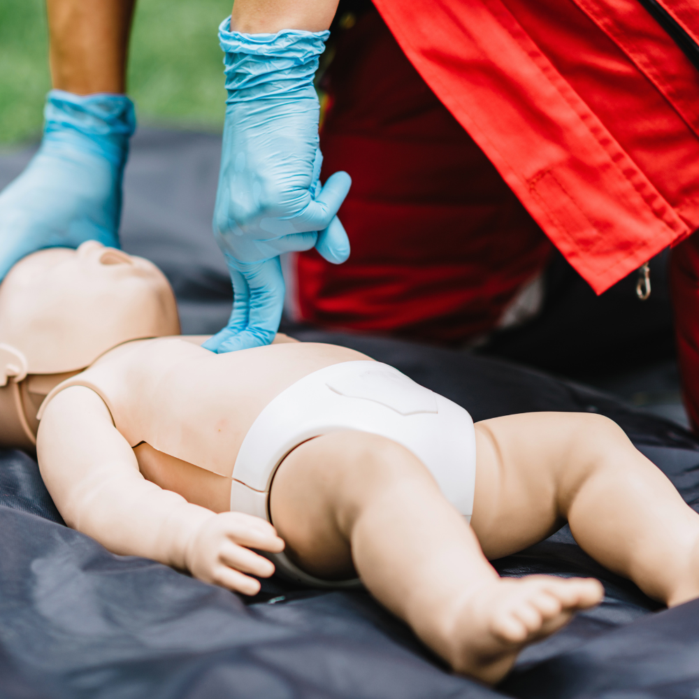 Person with gloves on hands giving an infant dummy chest compressions for CPR.