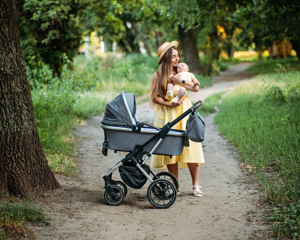 mom holding newborn baby outside with a stroller