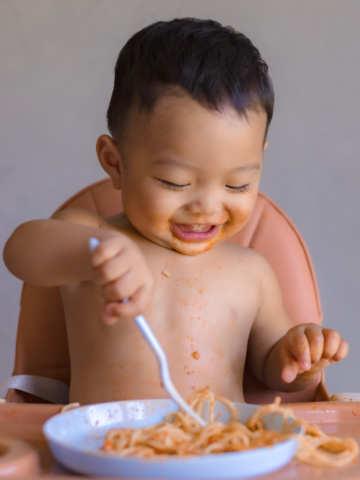baby eating spaghetti in a high chair