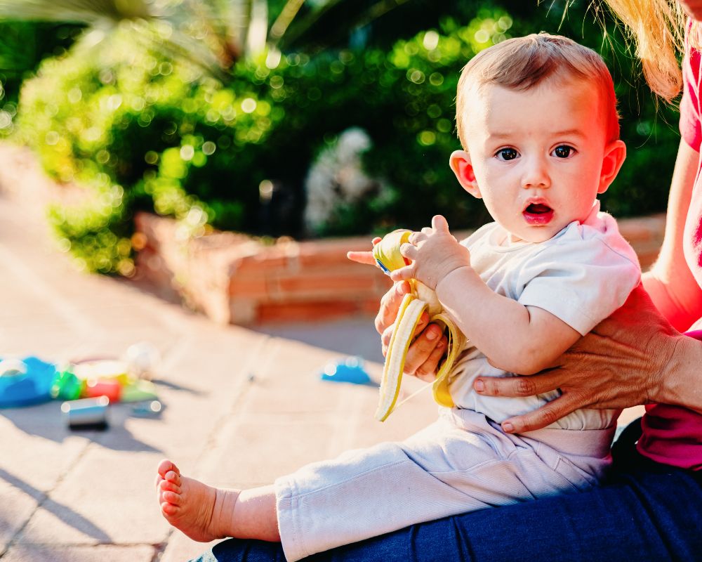 6 month old baby holding a banana and sitting outside