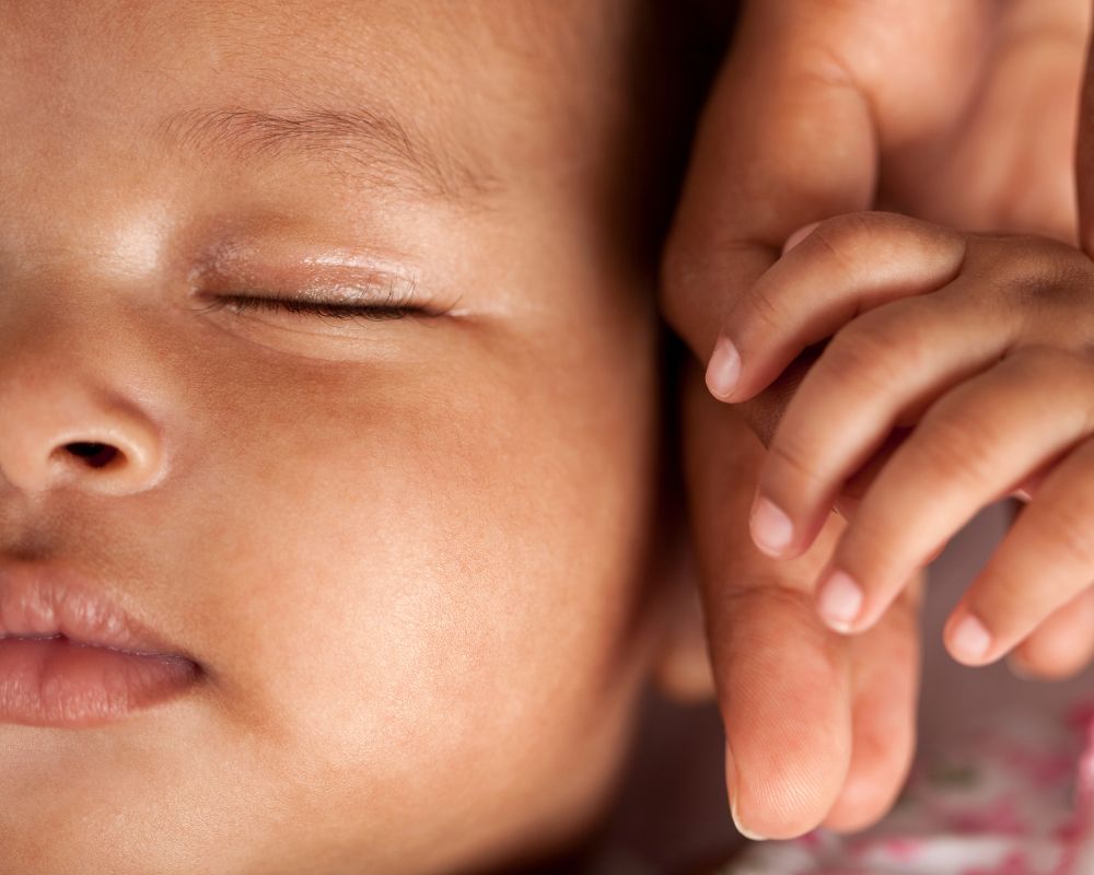 close-up of parent holding newborn's hand next to their face
