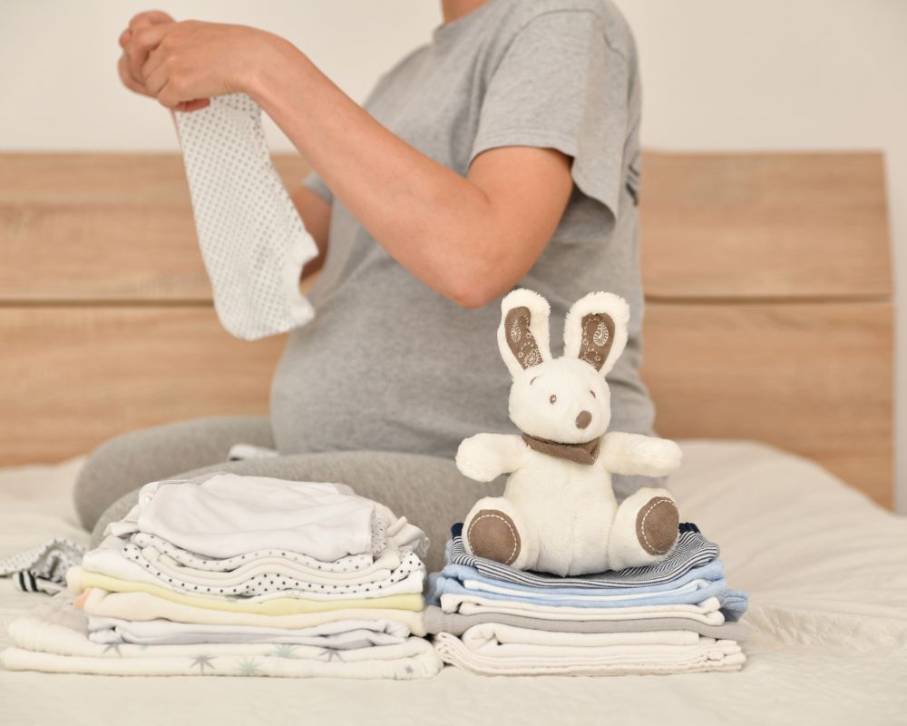 image of pregnant woman folding clothes including swaddles and sleep sacks