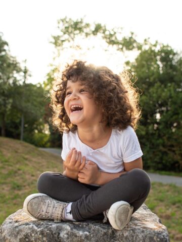 image of 4 year old sitting on rock giggling