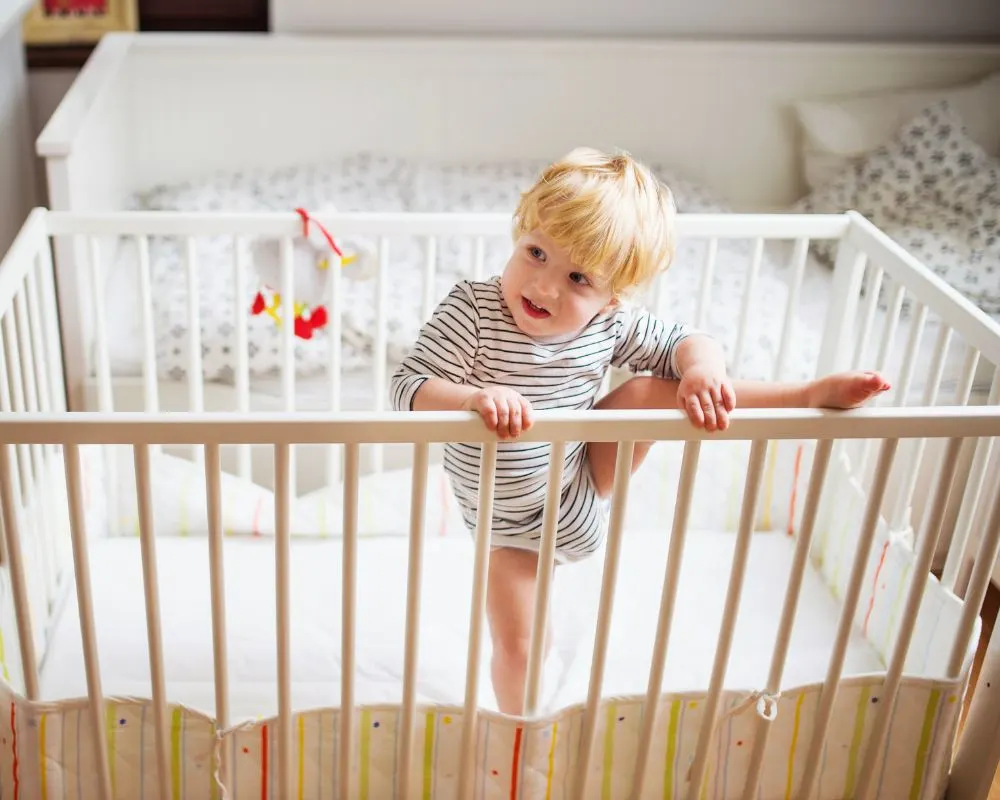 image of toddler standing in a crib with one leg up and over the top rail