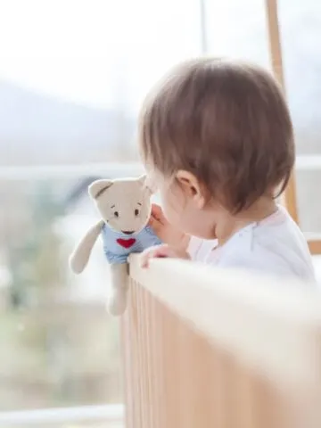 image of baby standing in crib holding a toy
