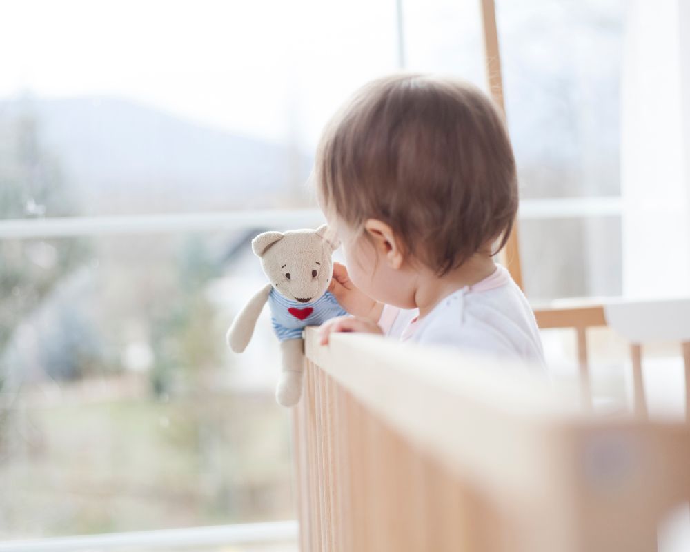 11 month old baby standing in crib holding a toy