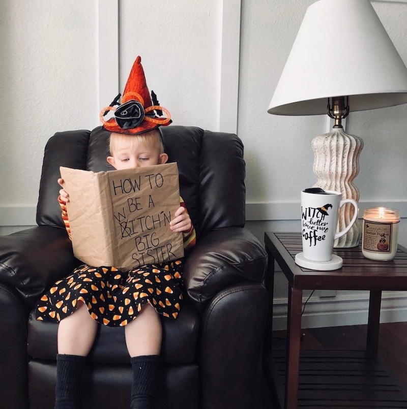 Halloween pregnancy announcement - Big sister dressed as a witch and reading book  how to be a witchin' big sister