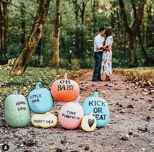 Halloween pregnancy announcement with colorful pumpkins and mom and dad in background