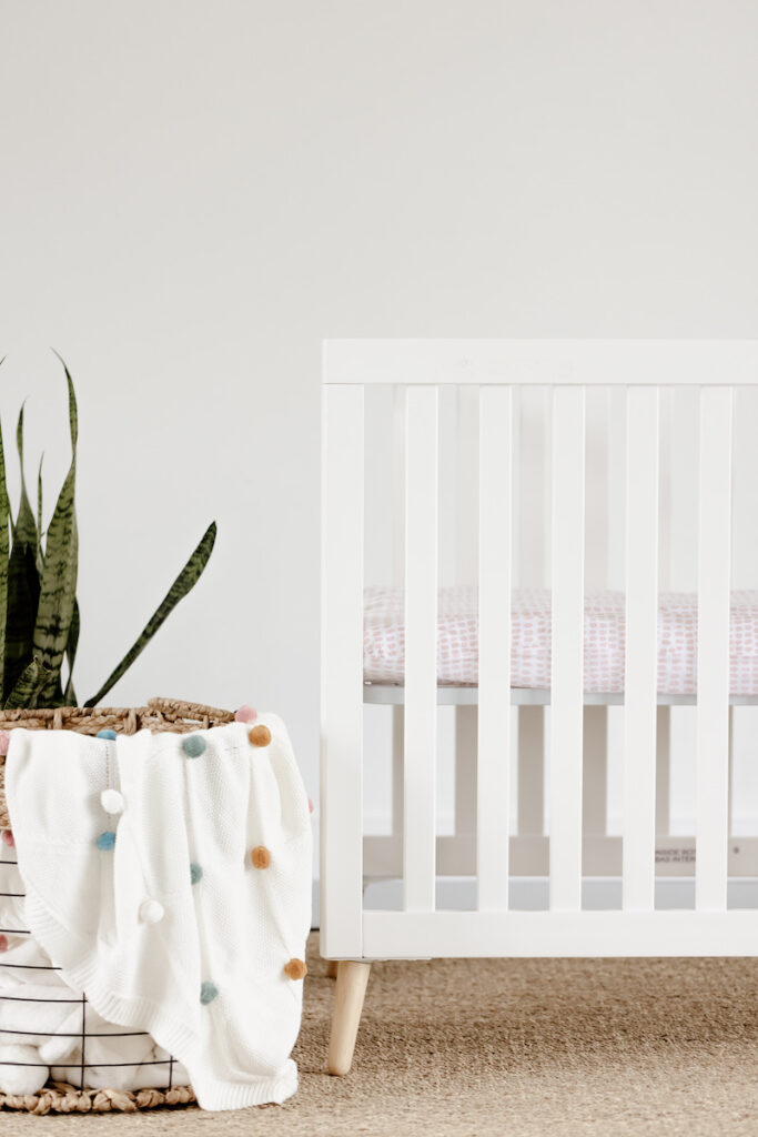 baby crib and plant with blanket basket nearby