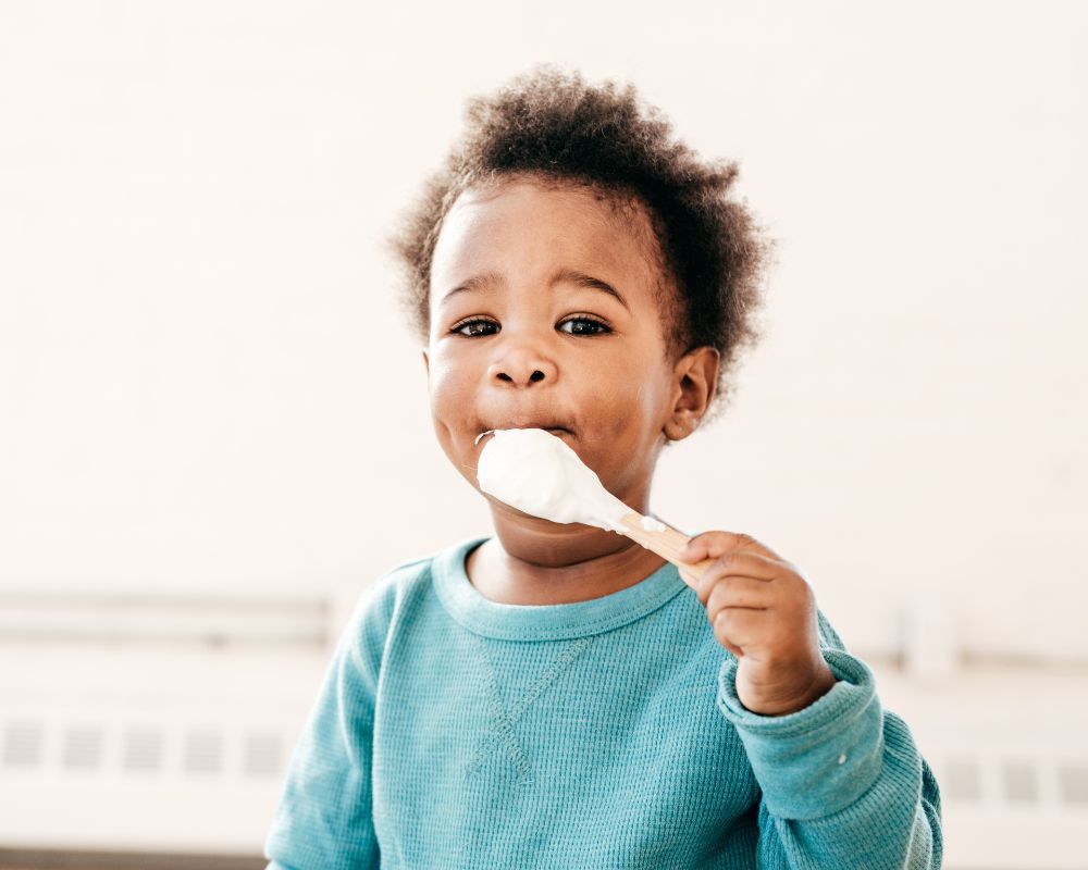 little boy holding a spoon with yogurt on it